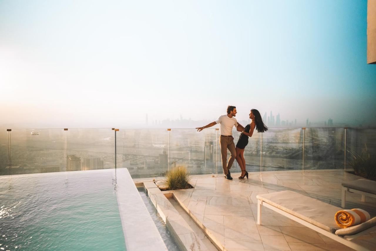 Five Jumeirah Village Дубай Экстерьер фото The image shows a couple dancing together on a terrace or balcony with a view of a city skyline in the background. They appear to be enjoying a romantic moment, surrounded by a luxurious setting that includes a swimming pool. The atmosphere is bright