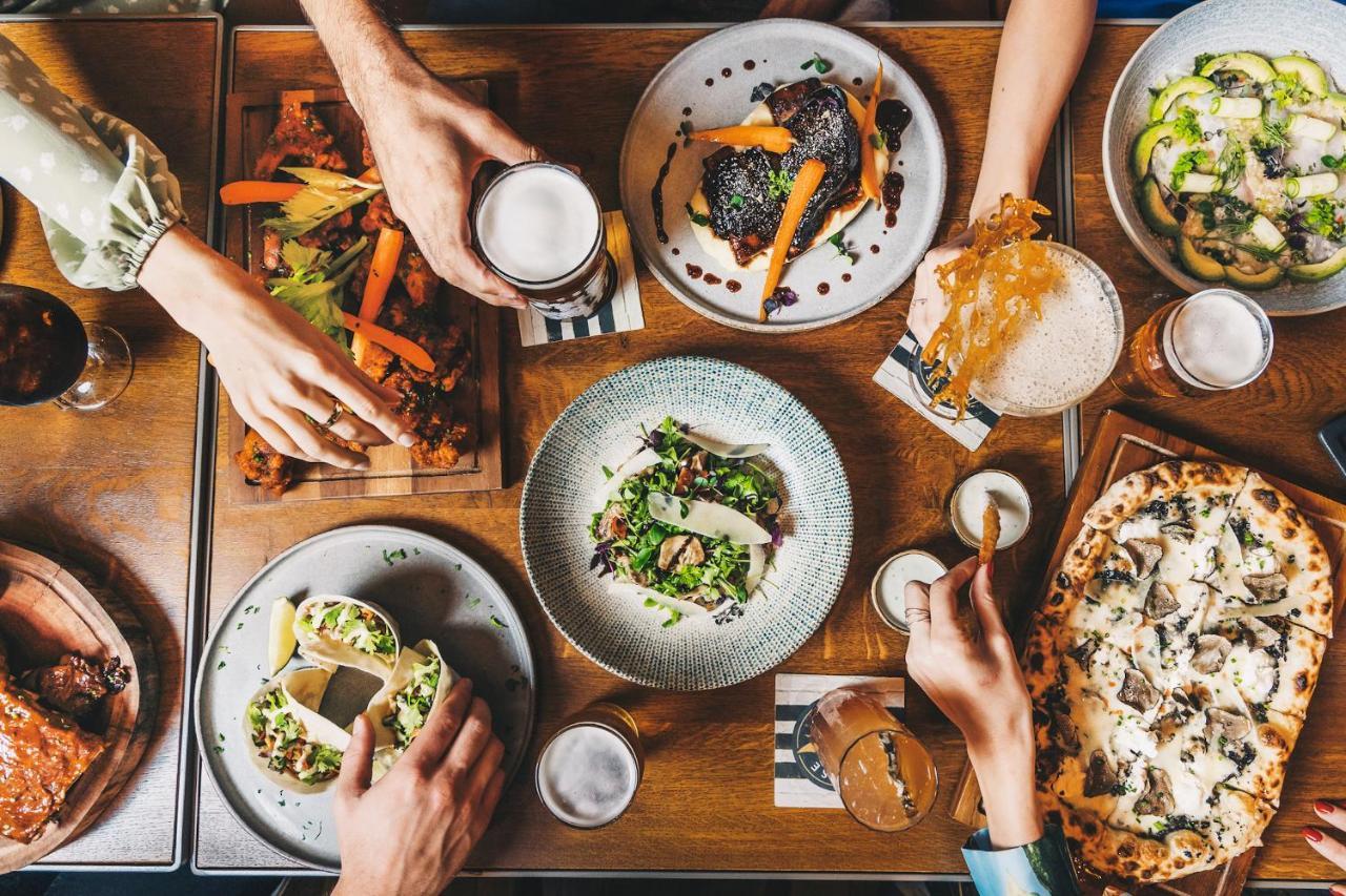 Five Jumeirah Village Дубай Экстерьер фото The photo displays a table filled with a variety of delicious food and drinks. There are several dishes, including a colorful salad in a round bowl, tacos, and what appears to be a pizza. On the side, there are also wooden platters with grilled veget