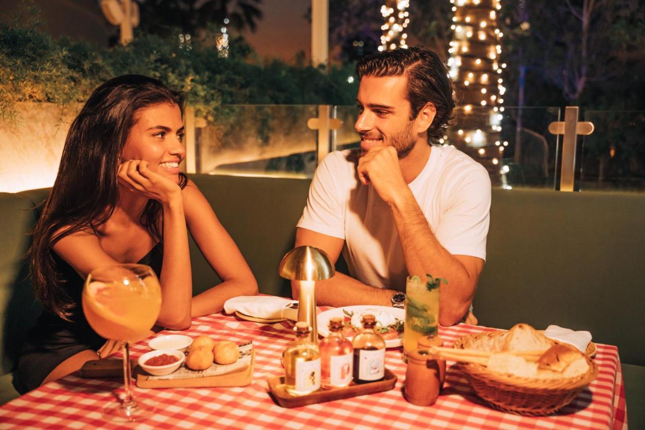 Five Jumeirah Village Дубай Экстерьер фото The photo shows a romantic dining scene featuring a couple at a table. The setting is illuminated with soft lights, creating a warm atmosphere. The table is adorned with a red and white checkered tablecloth, and various dishes are presented, includin