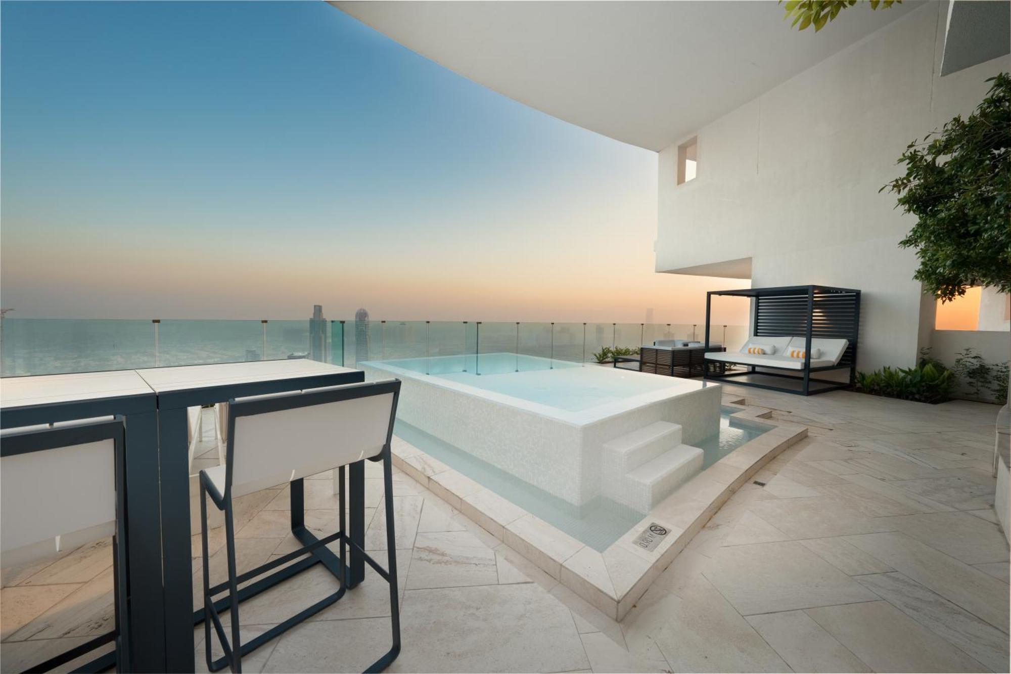 Five Jumeirah Village Дубай Экстерьер фото The photo depicts a luxurious outdoor space featuring a small infinity pool or hot tub that overlooks a scenic view. There is a stylish seating area nearby with modern furniture, including a table and chairs. The surroundings have a minimalist design