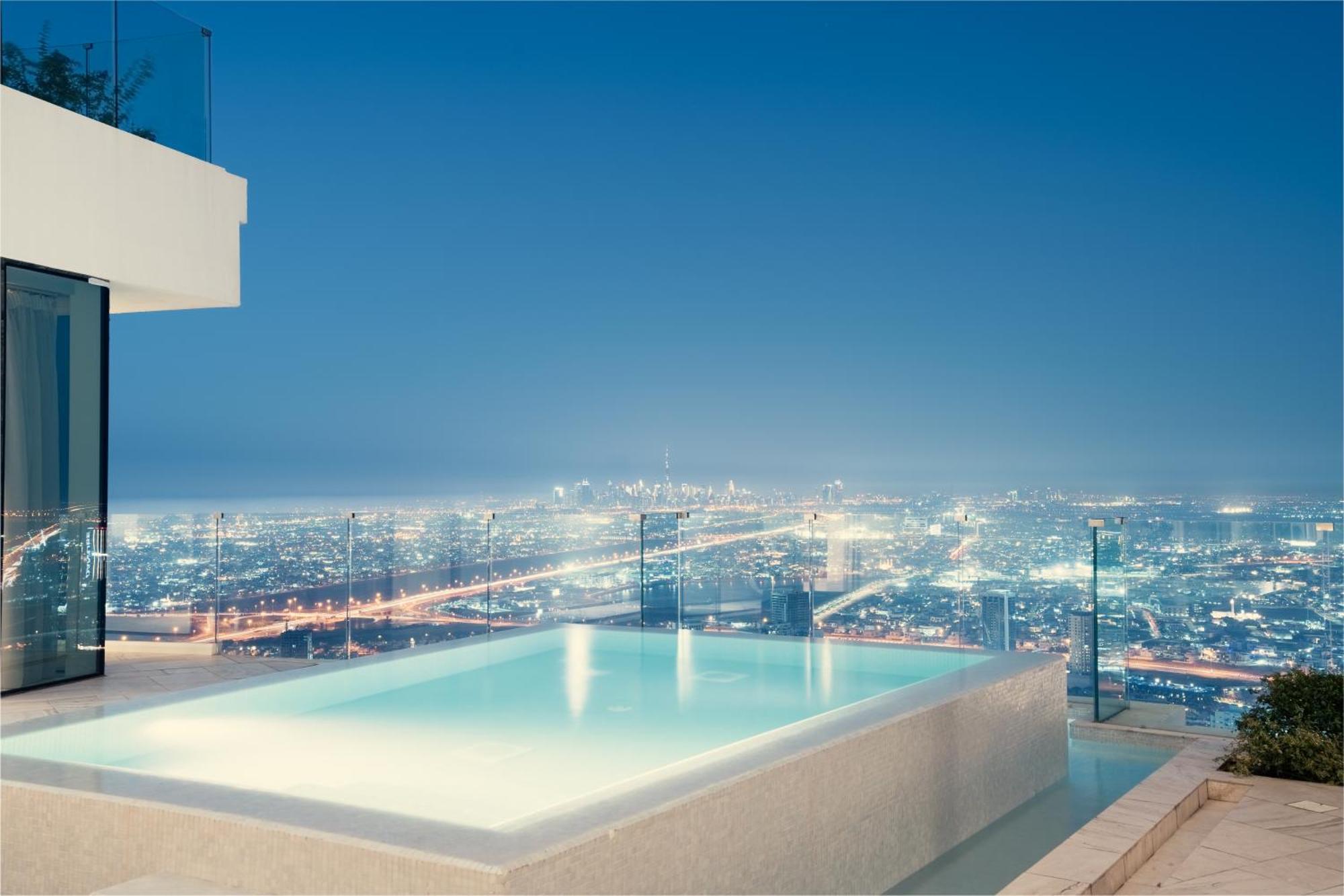 Five Jumeirah Village Дубай Экстерьер фото The photo showcases a luxurious infinity pool situated on an elevated terrace, overlooking a sprawling cityscape at night. The pool's water has a serene glow, reflecting the city lights below, which shimmer and create a vibrant backdrop. The architec