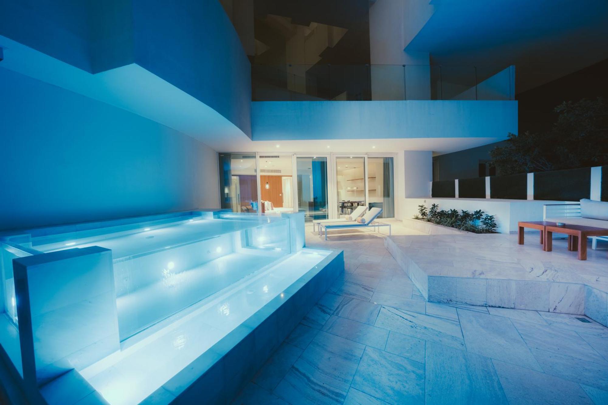 Five Jumeirah Village Дубай Экстерьер фото The photo shows a modern outdoor area, likely part of a contemporary home. It features a stylish, illuminated staircase leading down to a pool or water feature, with soft blue lighting that creates a serene atmosphere. In the background, large glass 