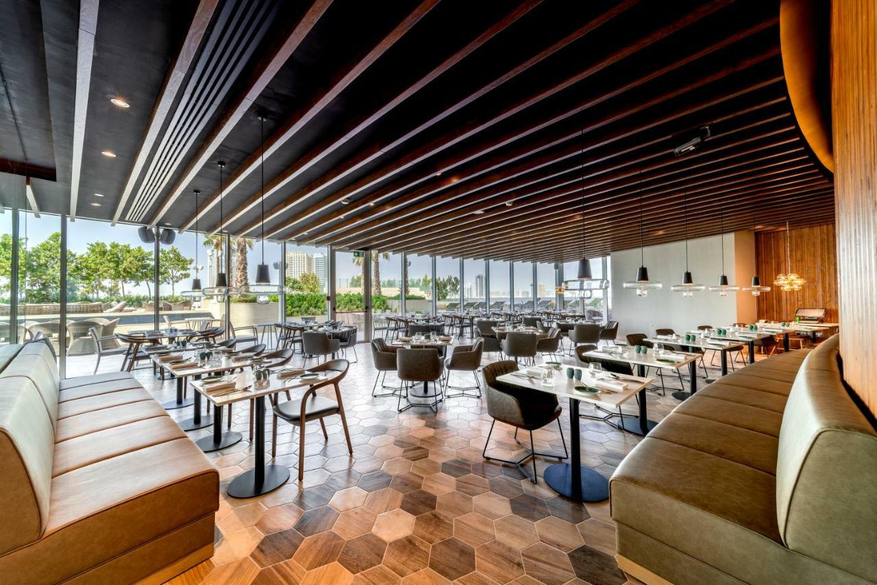 Five Jumeirah Village Дубай Экстерьер фото The photo shows the interior of a modern restaurant. It features a spacious layout with a combination of wooden and tiled flooring, characterized by hexagonal tiles. The ceiling has a modern design with wooden beams that add a sophisticated touch. Th